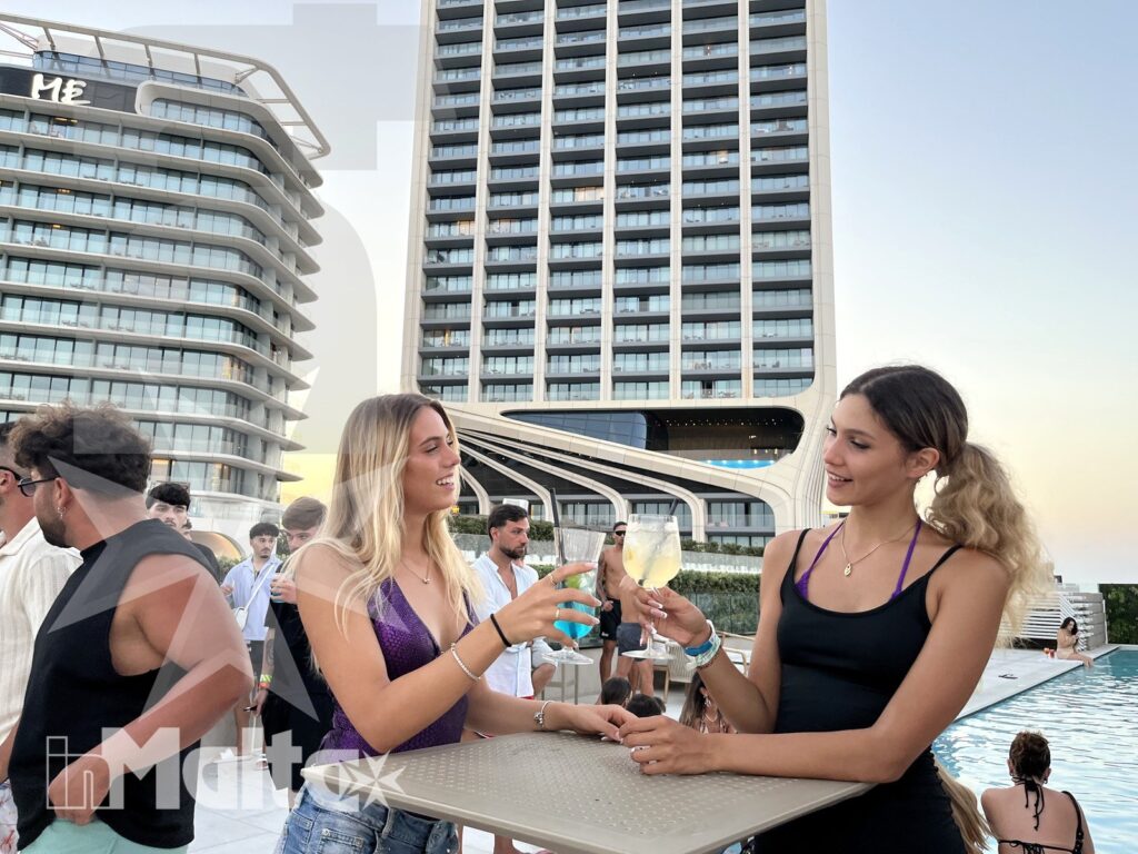 Two young women toast beside a modern rooftop pool while other course participants gather in the background during a study stay.